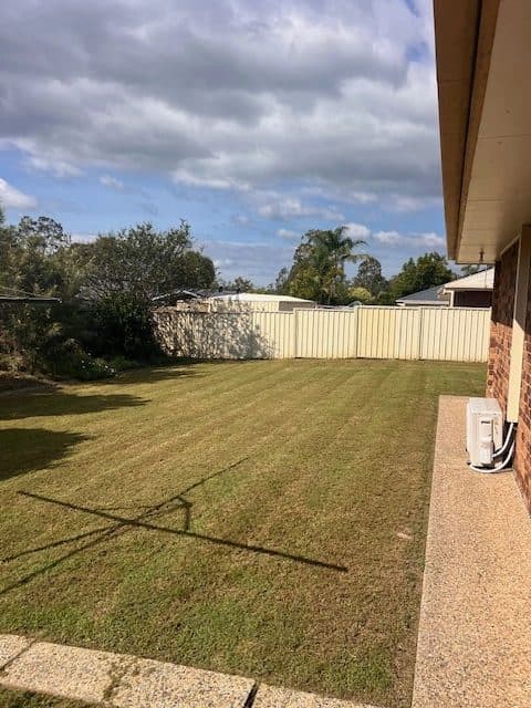 Neatly mown lawn beside a brick house and cream fence